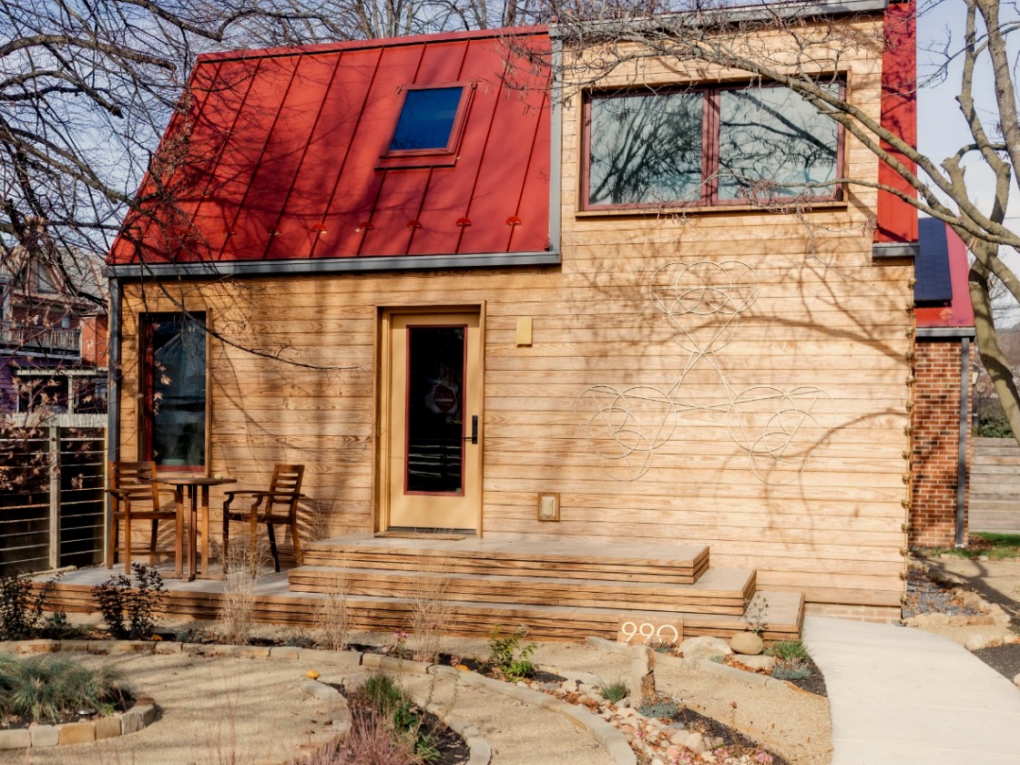 990 Oak Street passive house: Arbor Wood thermally modified wood siding in natural pine, standing-seam red metal roof, metal Sacred Geometry icon on the side wall, and a private front stoop above the spiral garden