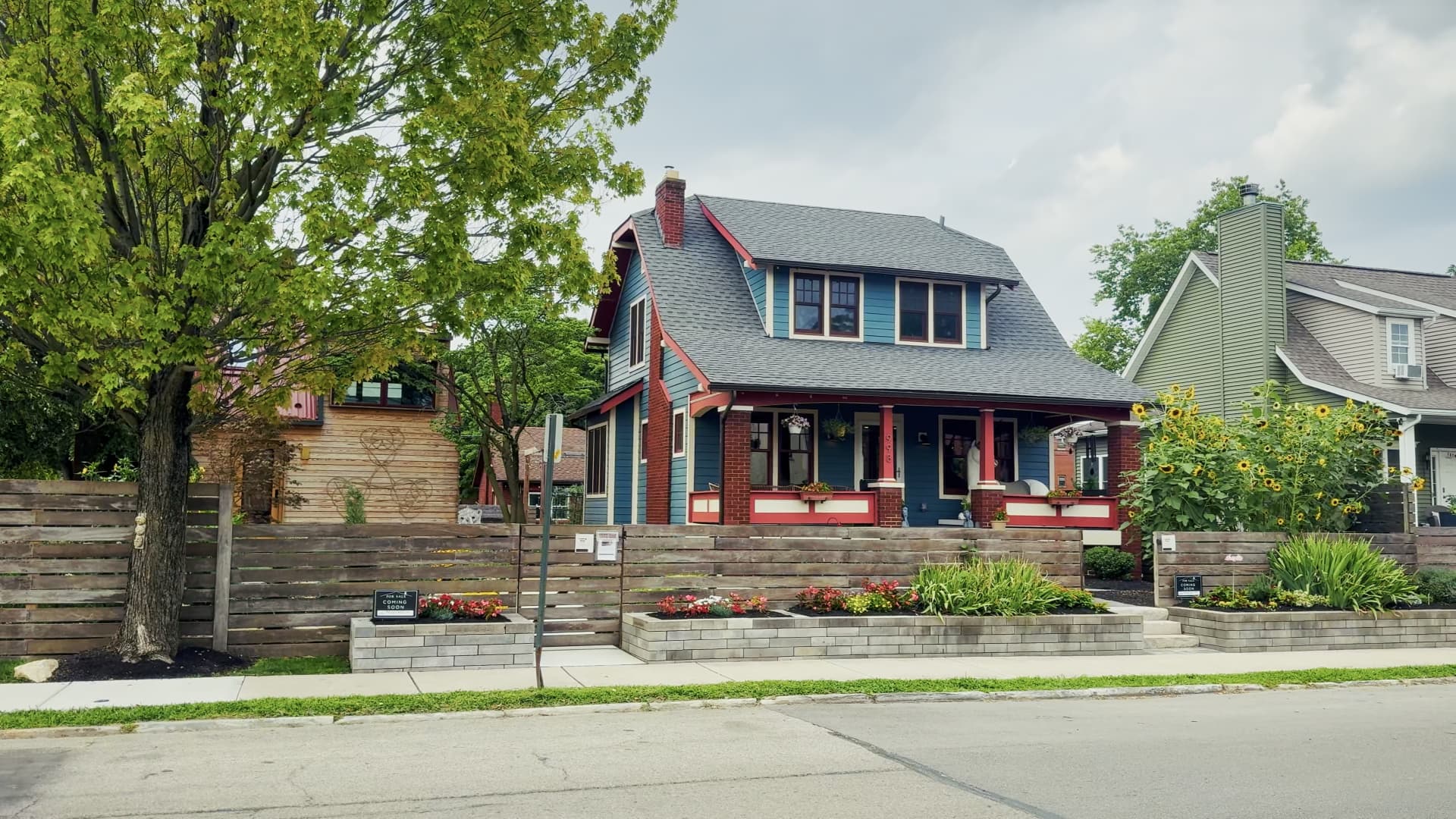 Street view of the teal main house with red trim seen behind a vertical-slat cumaru wood privacy fence
