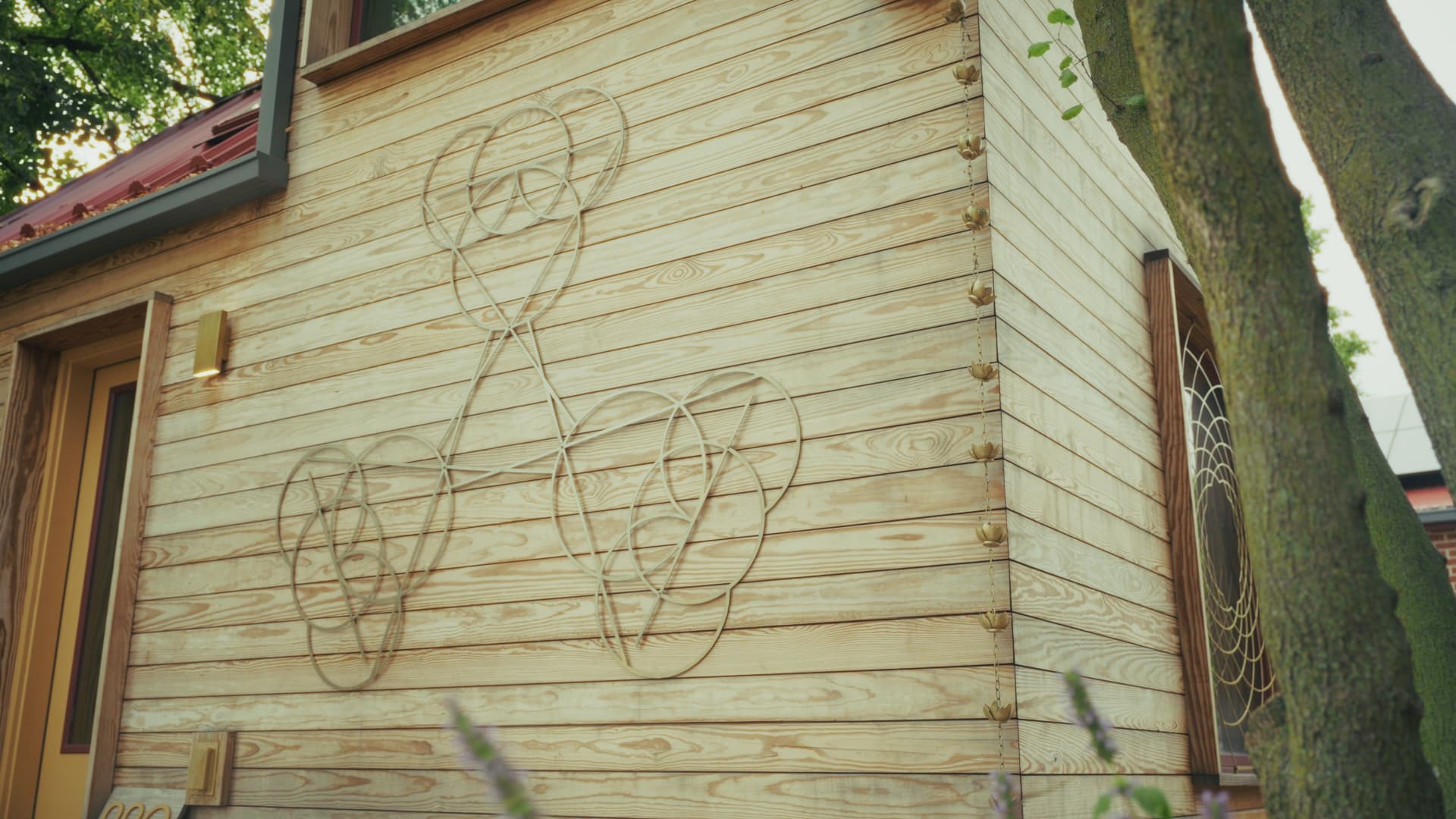 Close-up of Arbor Wood natural pine siding with metal wire sculptures mounted on it and a cast rain chain hanging at the corner