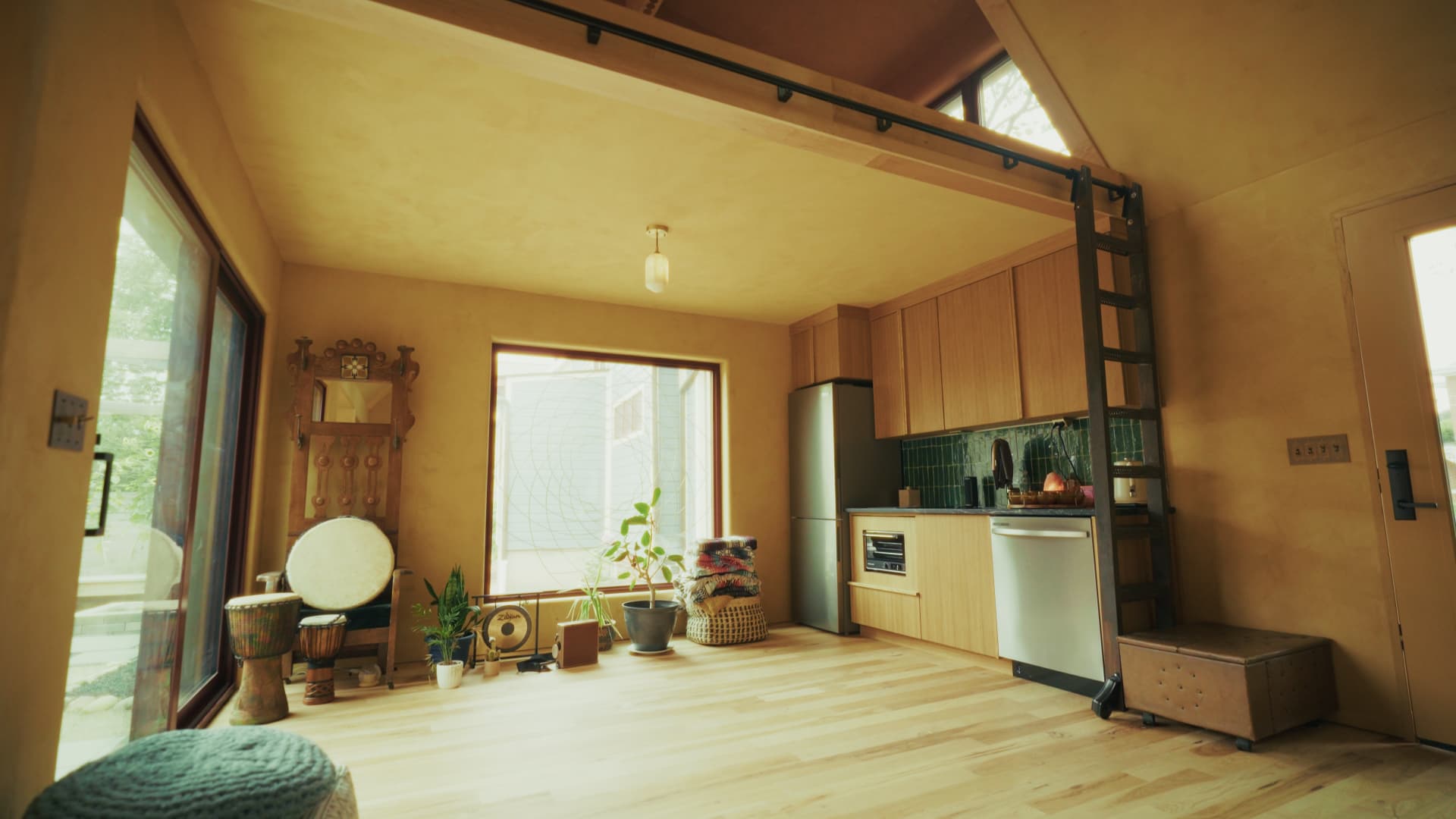 Open studio space with light wood floors, earthy plaster walls, and a sliding ladder up to the loft