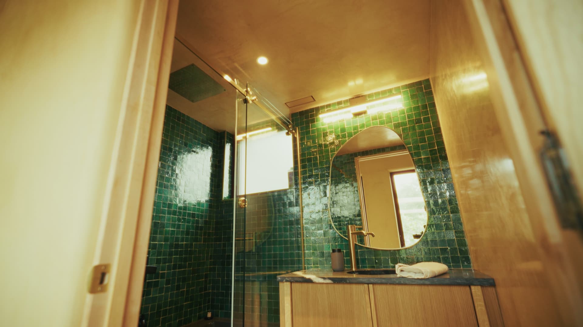 Passive house bathroom with vibrant handmade green square tile and a round modern mirror