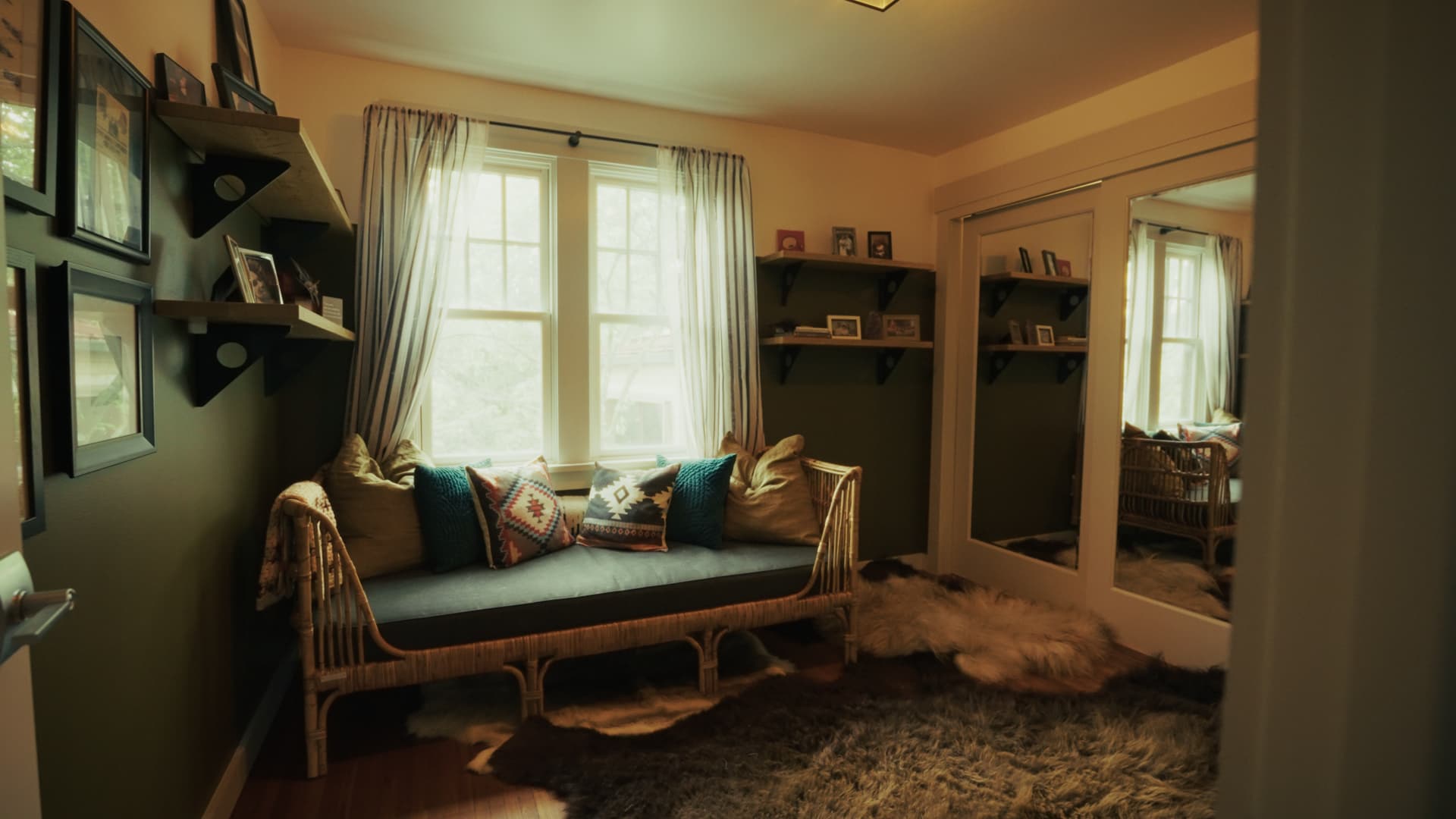 Room with green painted walls, a wicker daybed beneath a window, and sheepskin rugs on the floor