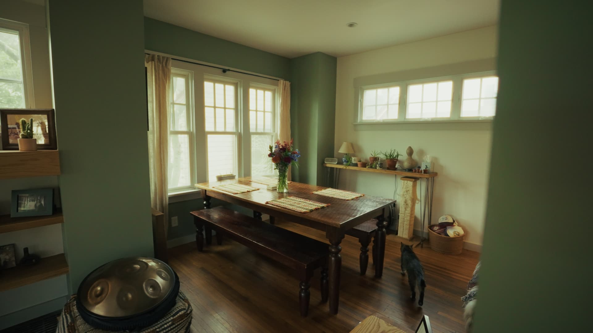Dining area with a large wooden table and bench seating set against a sage green wall
