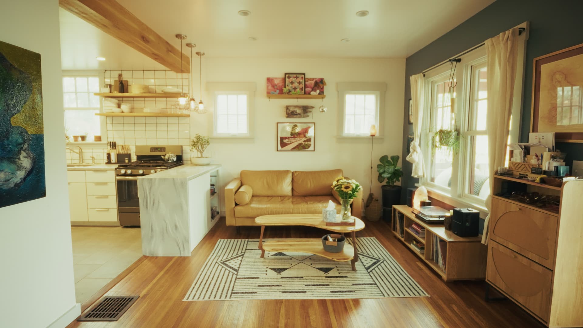 Living room with light walls, leather sofa, and an open sightline through to the kitchen beyond