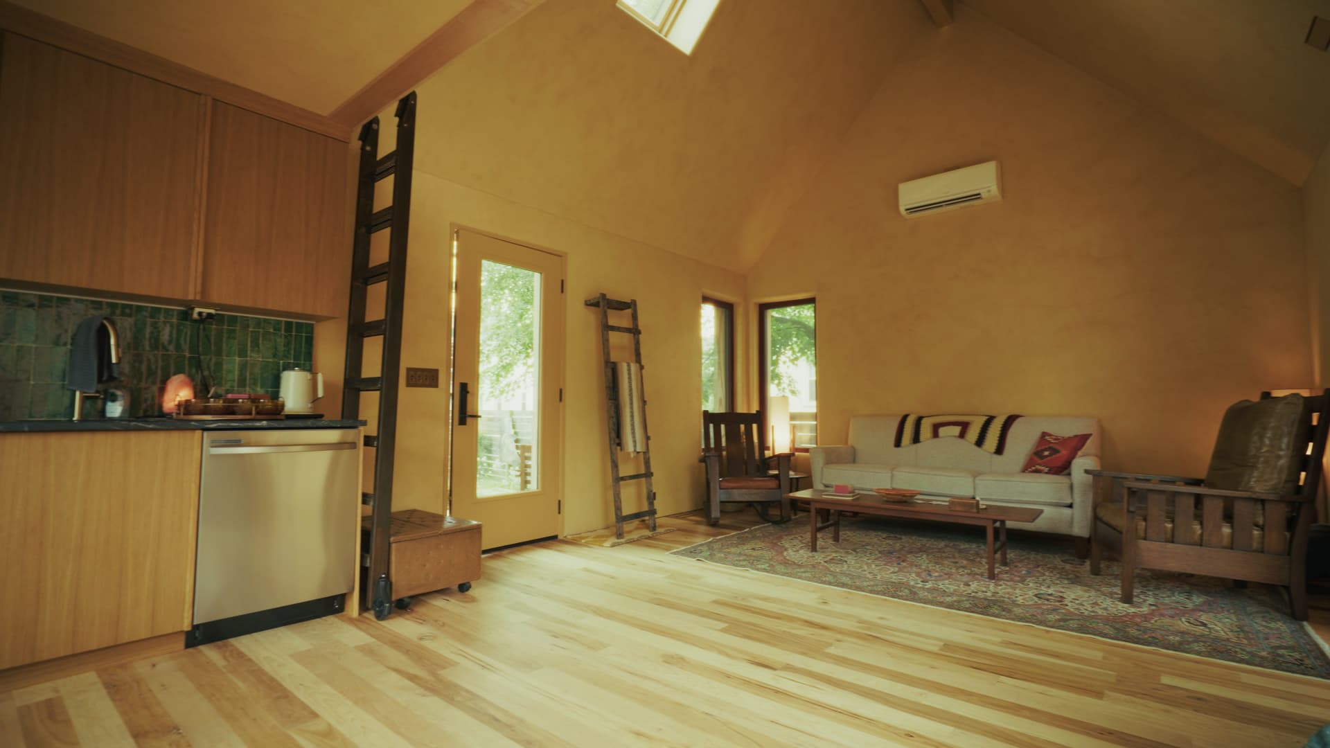 Studio interior of the passive house with high ceilings, earthen plaster walls, a sofa, and a sliding loft ladder