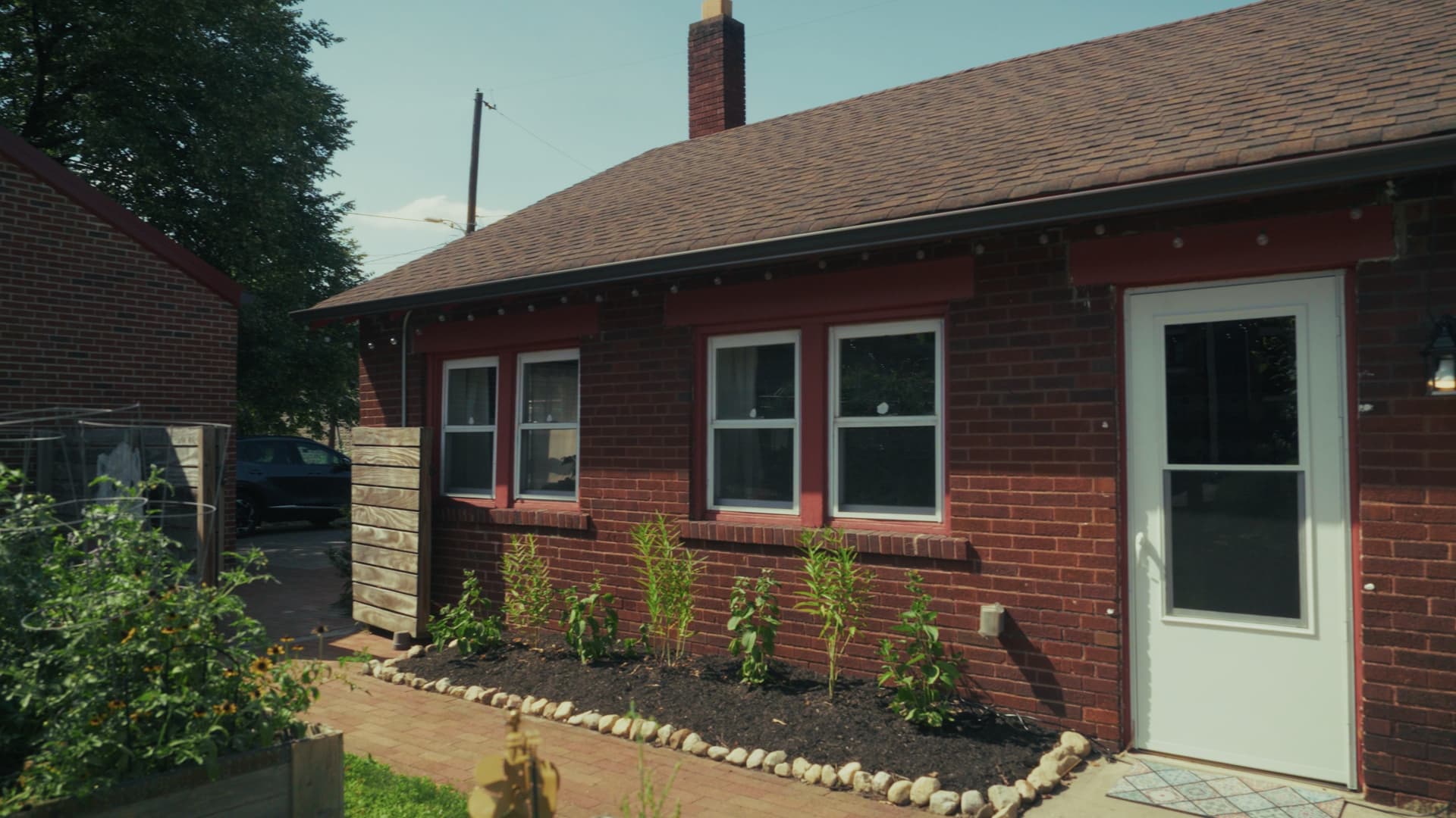 Exterior of the brick carriage house at 998 Oak: white doors and windows, a planted bed along the foundation, and a paver walk leading to its private entrance