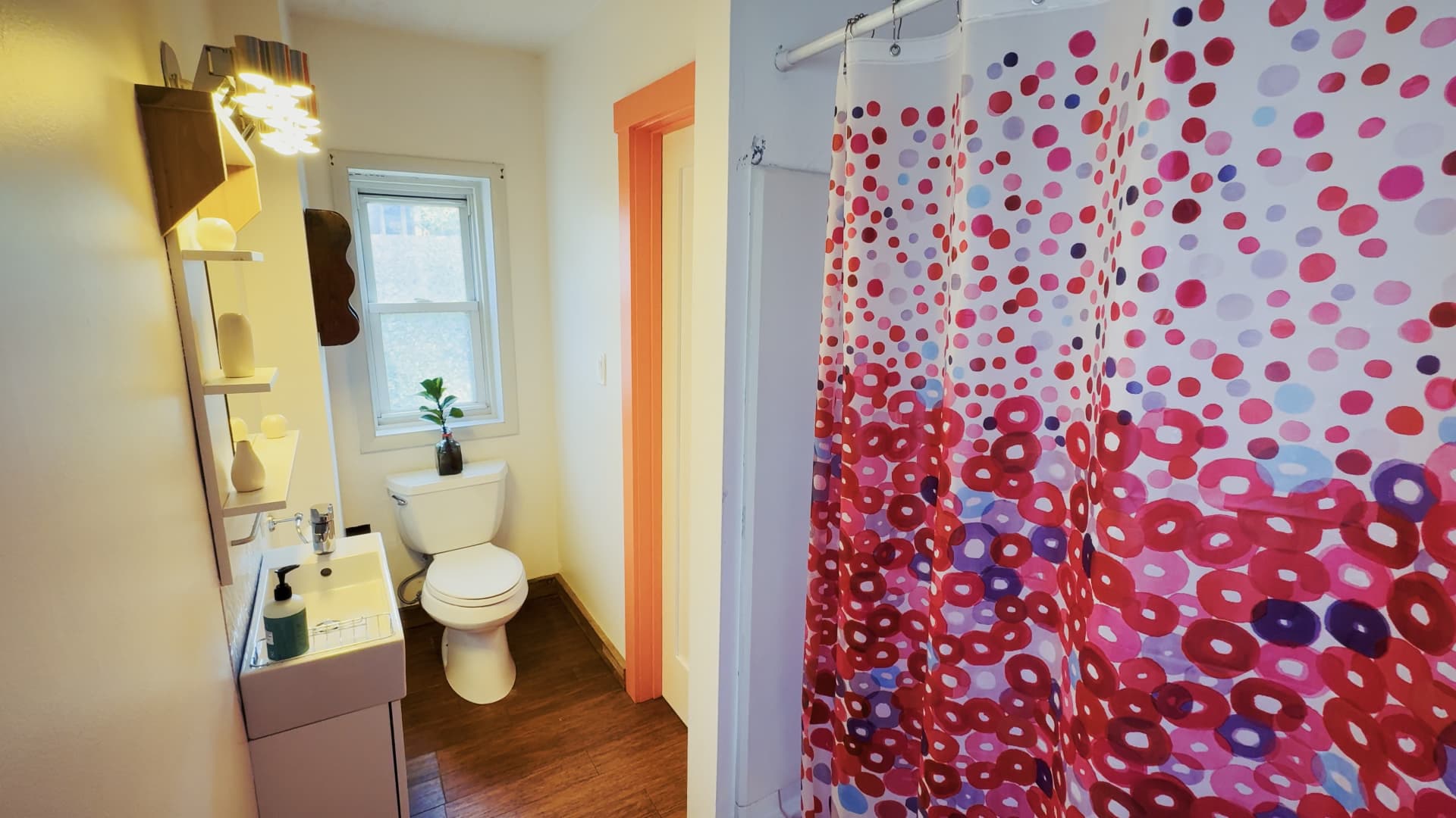 Full bathroom in the carriage house with orange painted door trim and a colorful polka-dot shower curtain