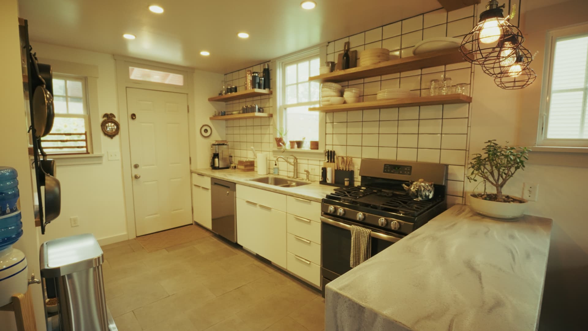 Main house kitchen with white cabinetry, white oak open shelving, subway tile backsplash, and Corian counters