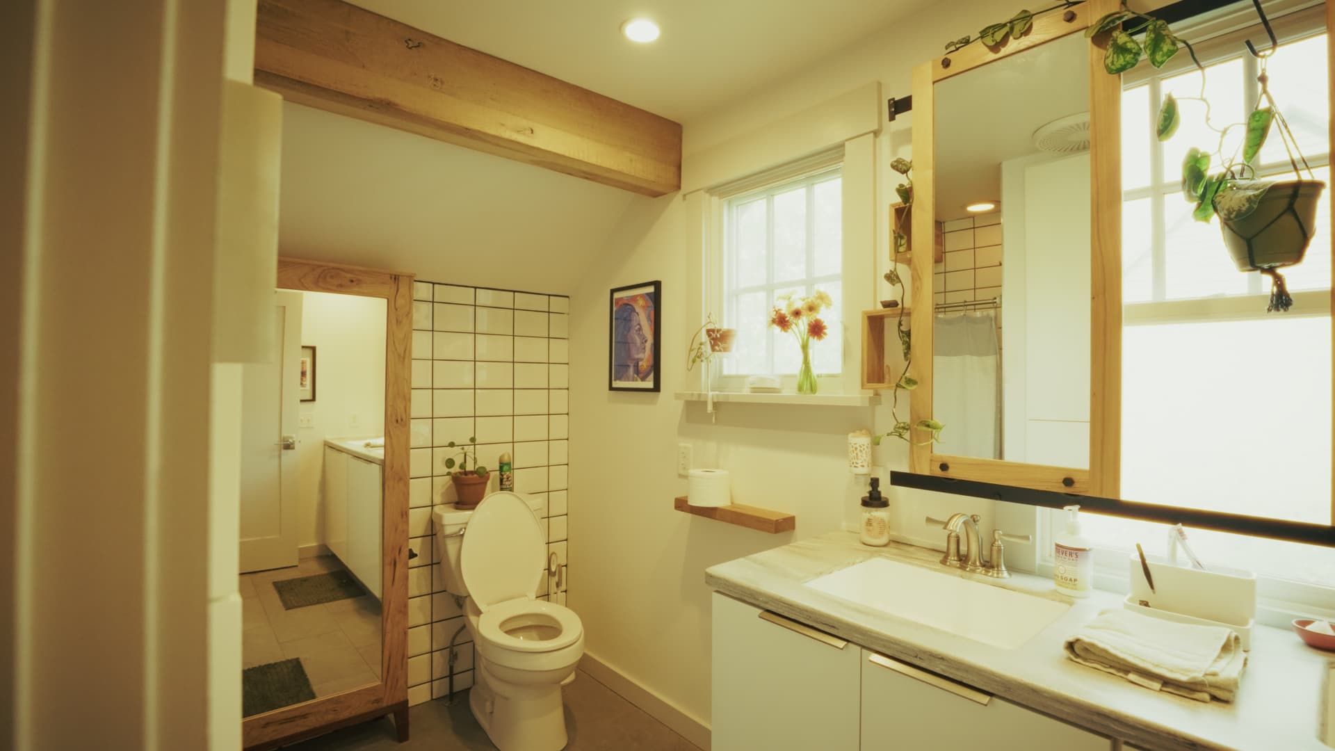 Bright bathroom with a white vanity, exposed wood beams overhead, and a large mirror