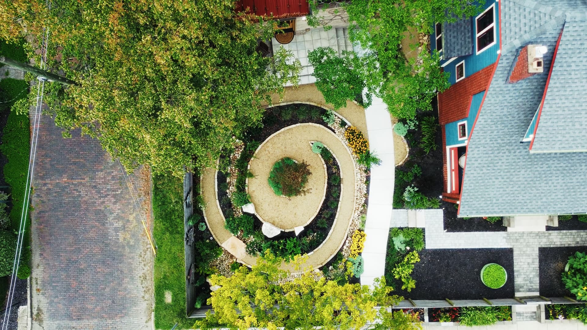 Overhead view of the gravel and stone spiral garden, concentric stone-edged beds radiating from a central Japanese maple with native pollinator plantings between them