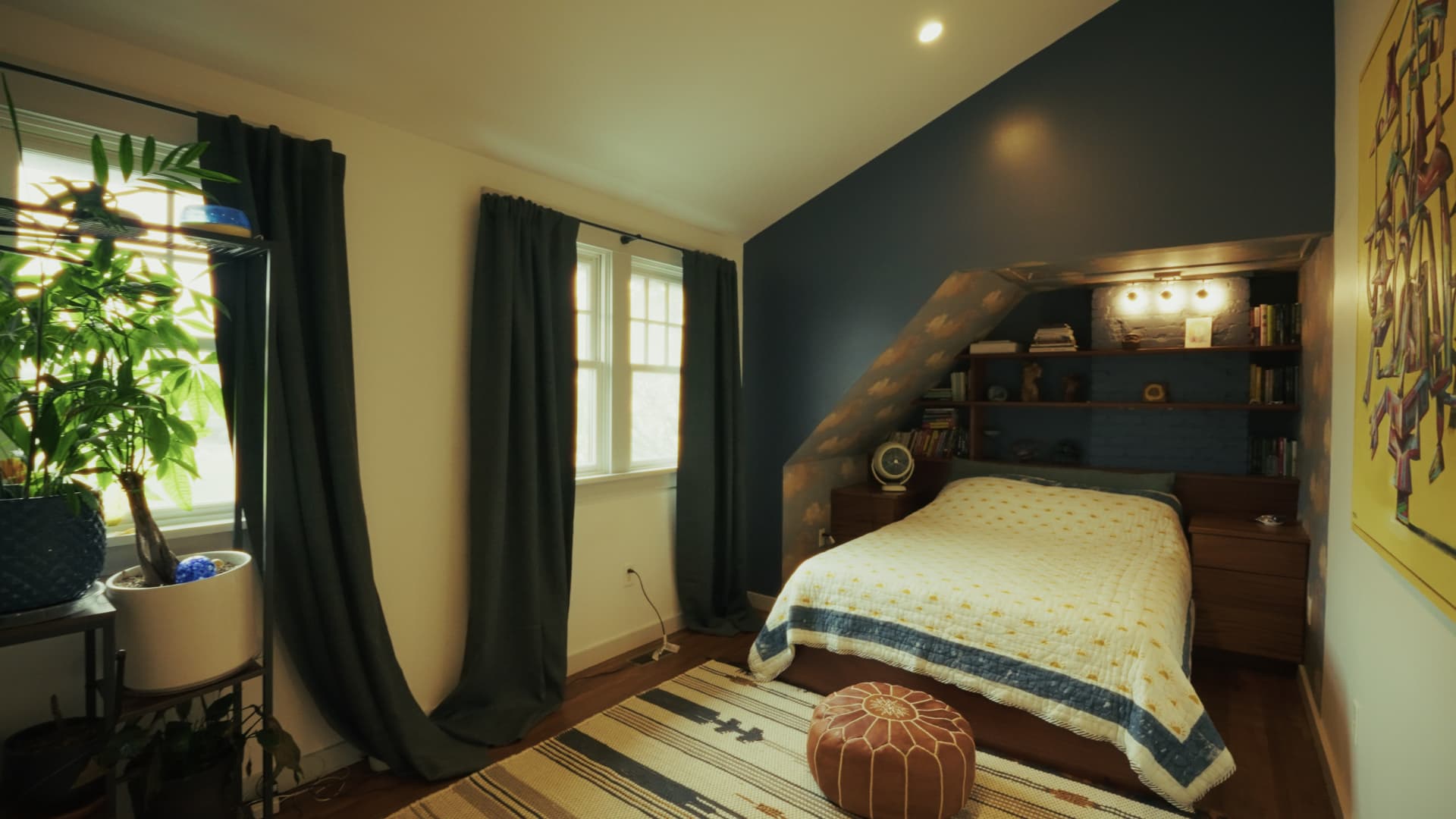 Bedroom with a vaulted ceiling, dark blue accent wall, quarter-sawn built-in shelving, and a patterned quilt on the bed