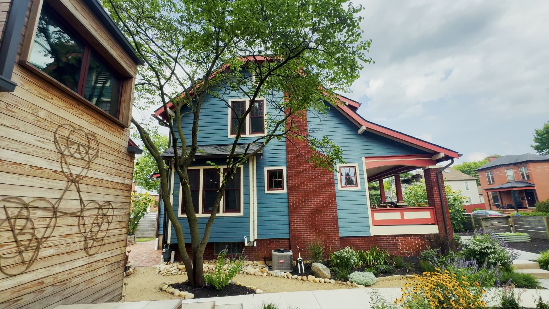 Side elevation of the teal main house showing the red brick chimney, exterior mechanicals, and side yard plantings