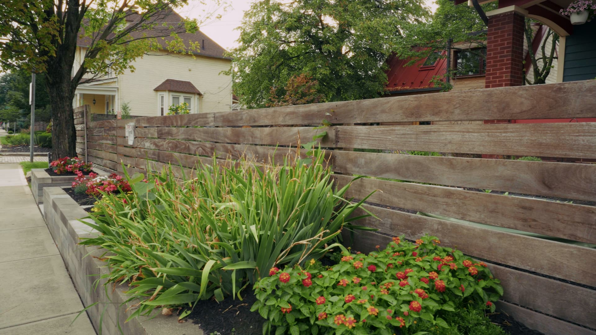 Vertical-slat cumaru privacy fence with flowers in a planter bed at its base